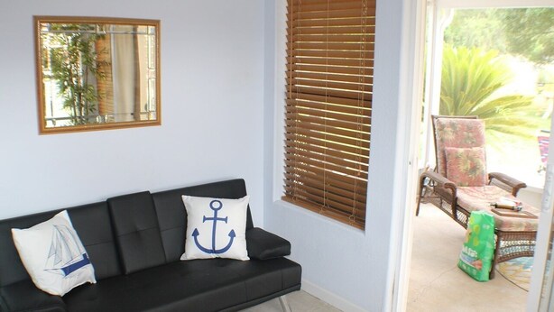 A black sofa with two pillows, one with an anchor design, and a window with blinds. - Navarre Beach Escape-Pet & Family Friendly (Navarre)