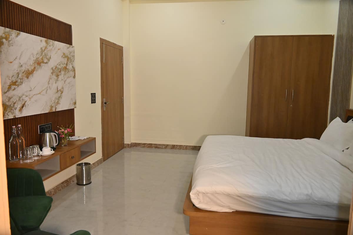 Une chambre d’hôtel avec un lit, une armoire en bois, un bureau avec une machine à café et une chaise verte.