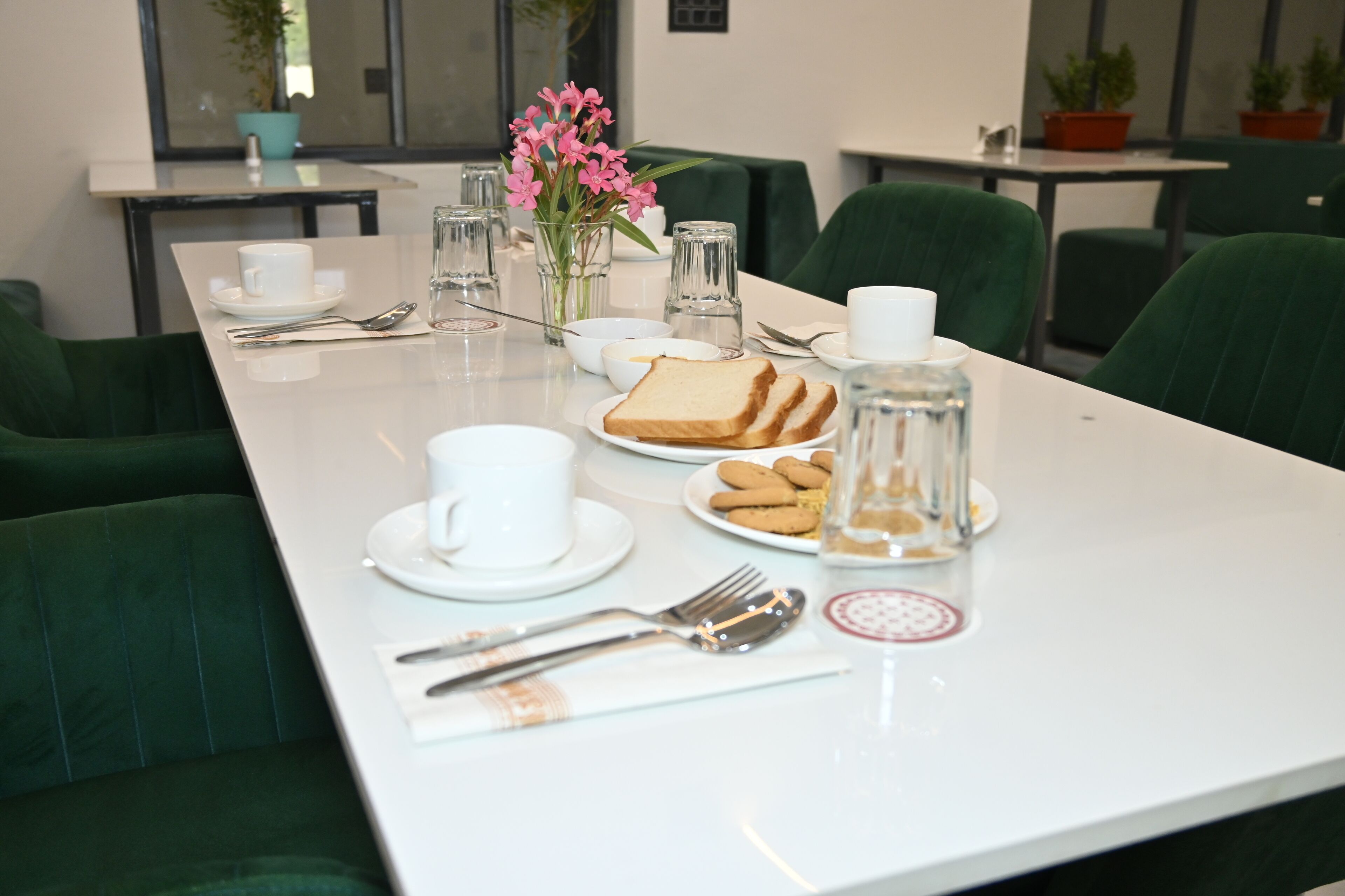 A neatly arranged dining table with a white tablecloth, green upholstered chairs, and a vase of pink flowers.