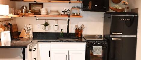 A kitchen with white cabinets, a black stove, a black refrigerator, and wooden shelves with various kitchen items.