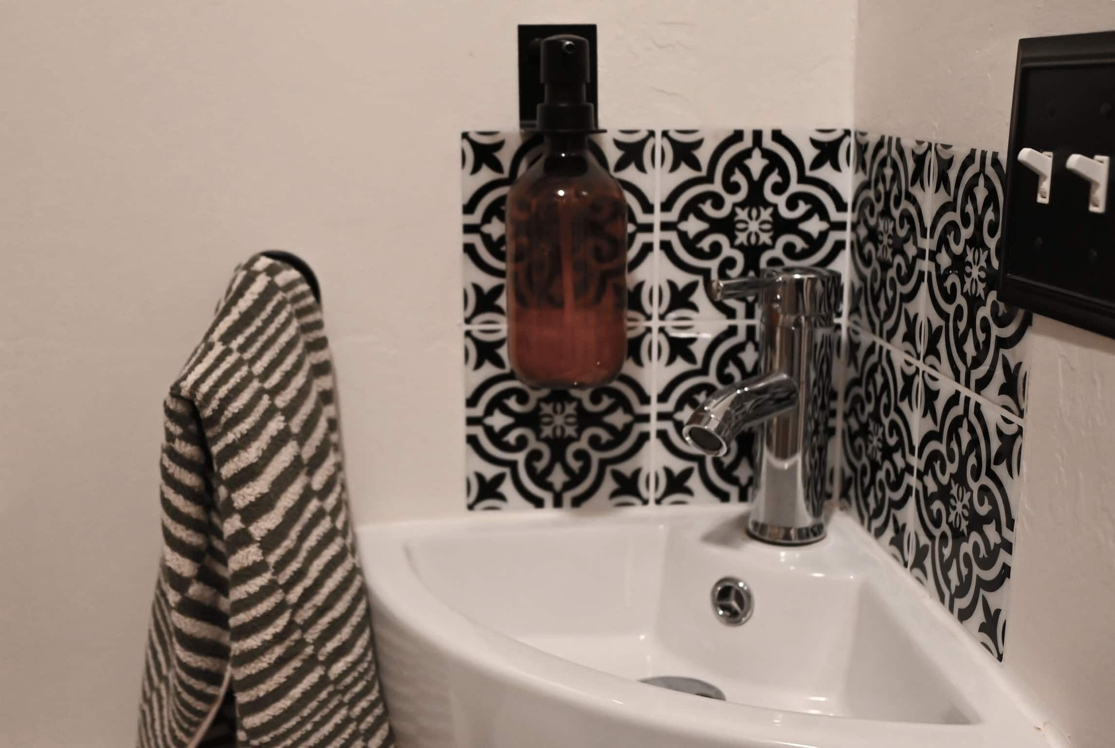 Un baño con un lavamanos blanco, un pared con diseño blanco y negro, y una toalla a rayas colgada en la pared.