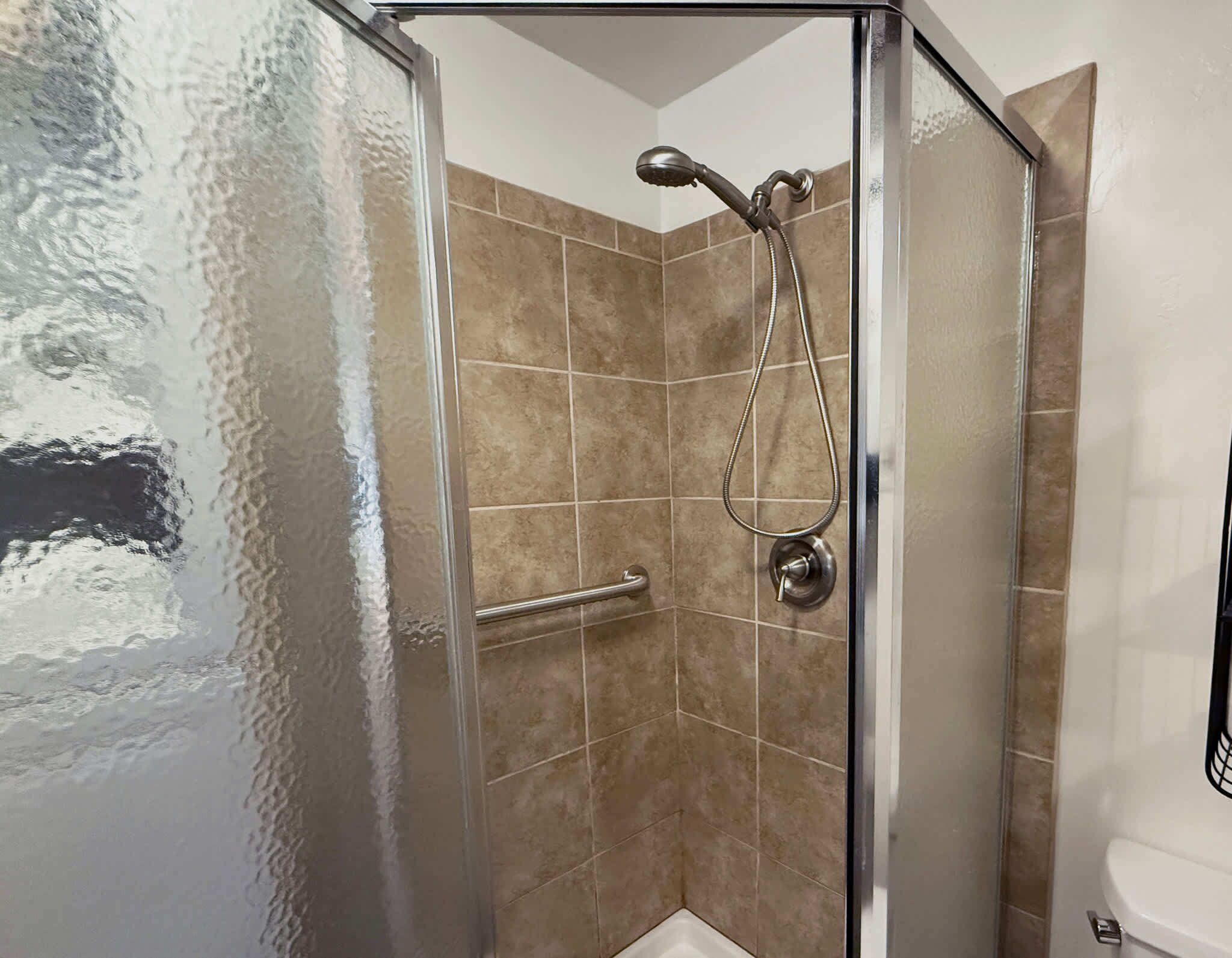 Une douche fermée par des parois en verre, dotée d’un pommeau de douche à main et d’un flexible de douche à main.