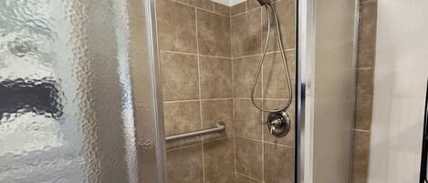 Une douche fermée par des parois en verre, dotée d’un pommeau de douche à main et d’un flexible de douche à main.