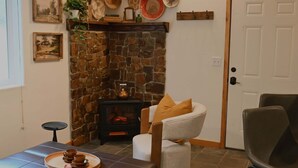 Un salon chaleureux avec une cheminée en pierre, un poêle à bois noir et un coin repas agrémenté d’un plateau de tasses.