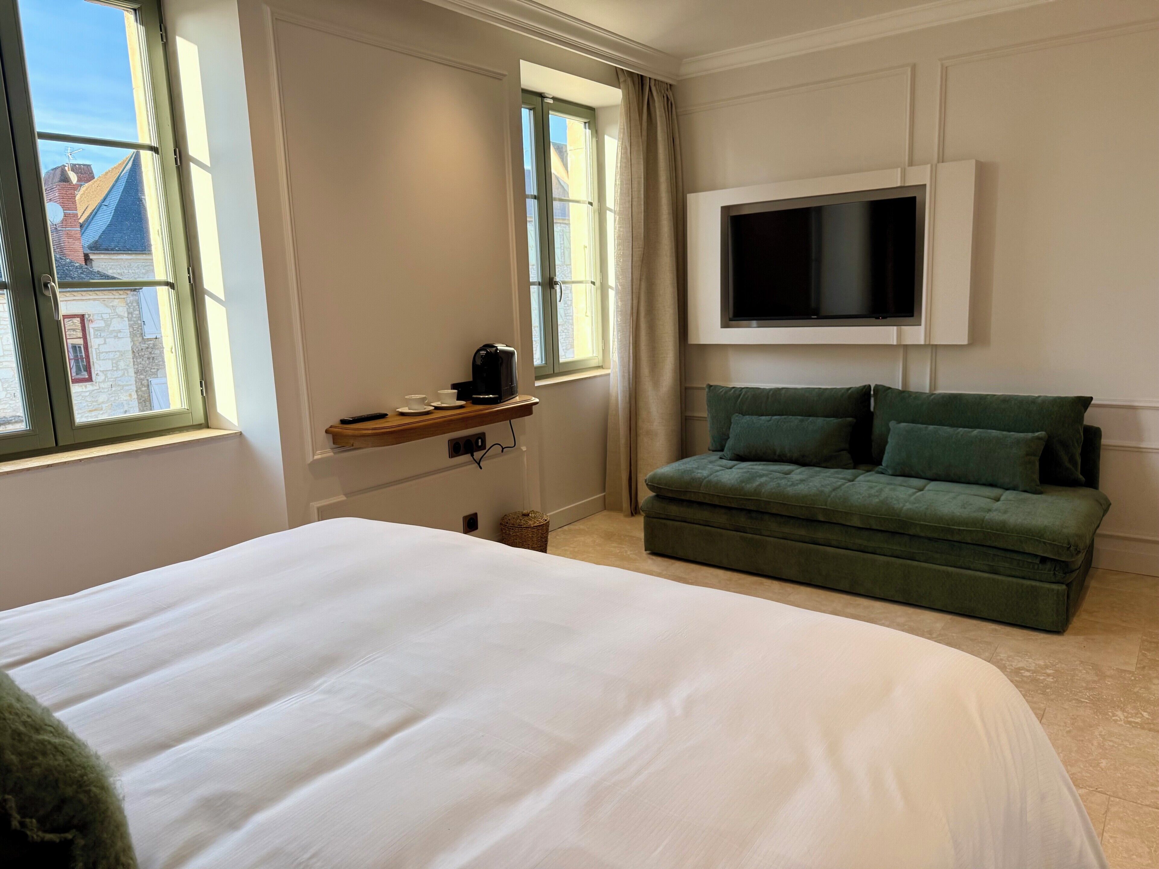 Een hotelkamer met een bed, een aan de muur bevestigde televisie, een bank en een raam met gordijnen.