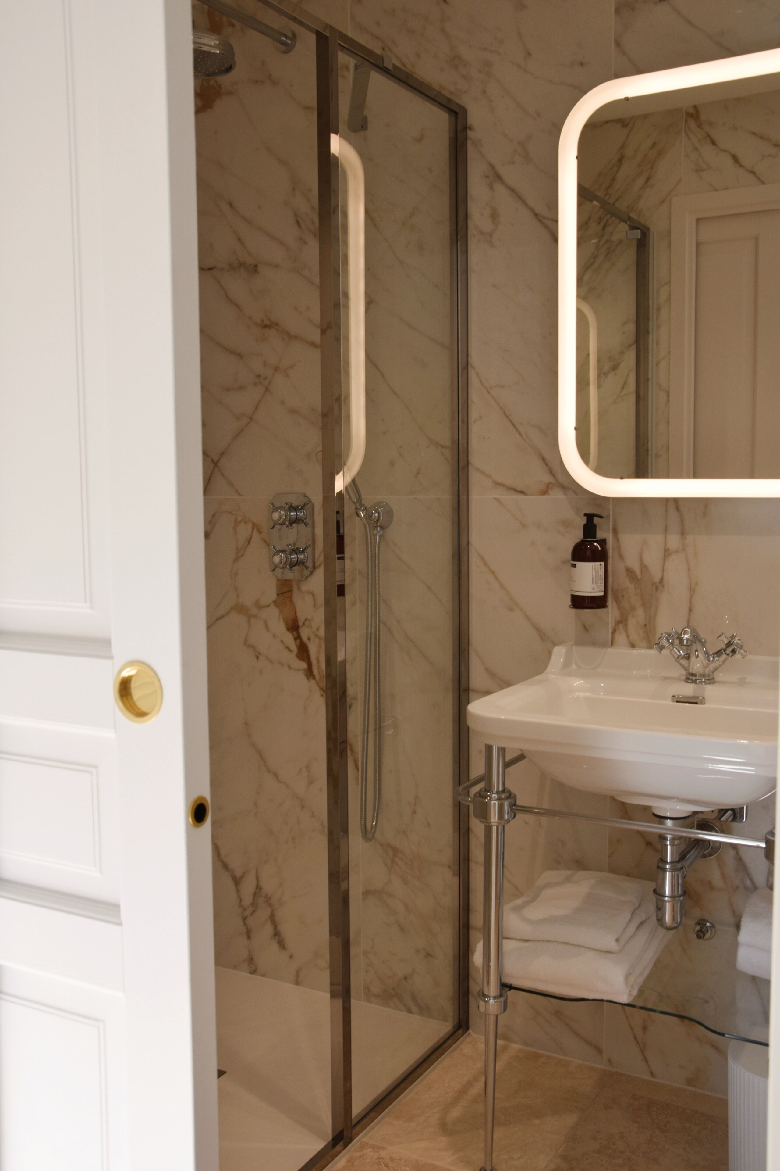 Een badkamer met een douchecabine van glas, een wit wastafelmeubel en een wand betegeld met marmer.