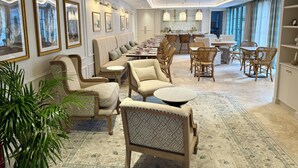 A spacious hotel lobby with a long sofa, dining area, and a large window with curtains. - Hotel Maison Turenne (Martel)