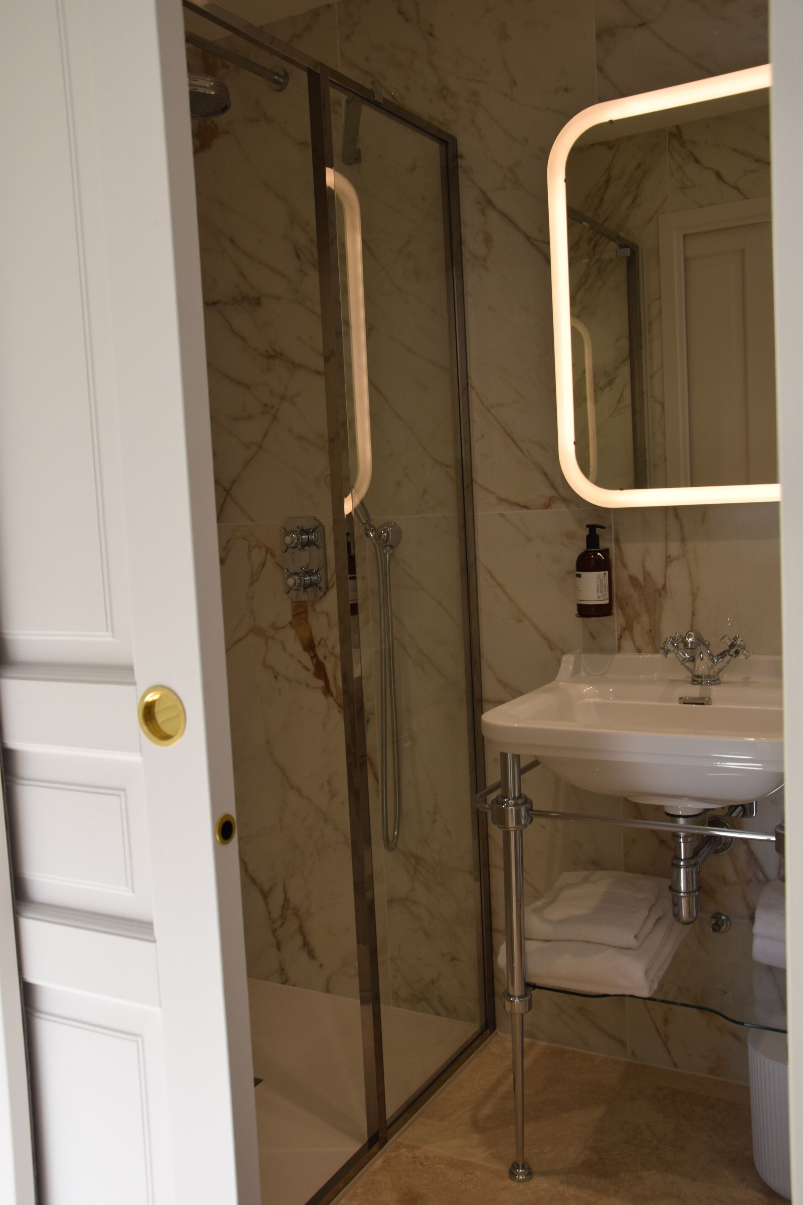 Un baño con cabina de ducha de vidrio, un lavamanos blanco y pared de mármol.