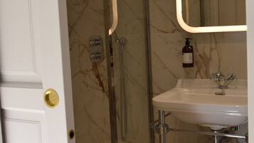 Une salle de bain avec une douche à parois de verre, un lavabo blanc et un mur en marbre.