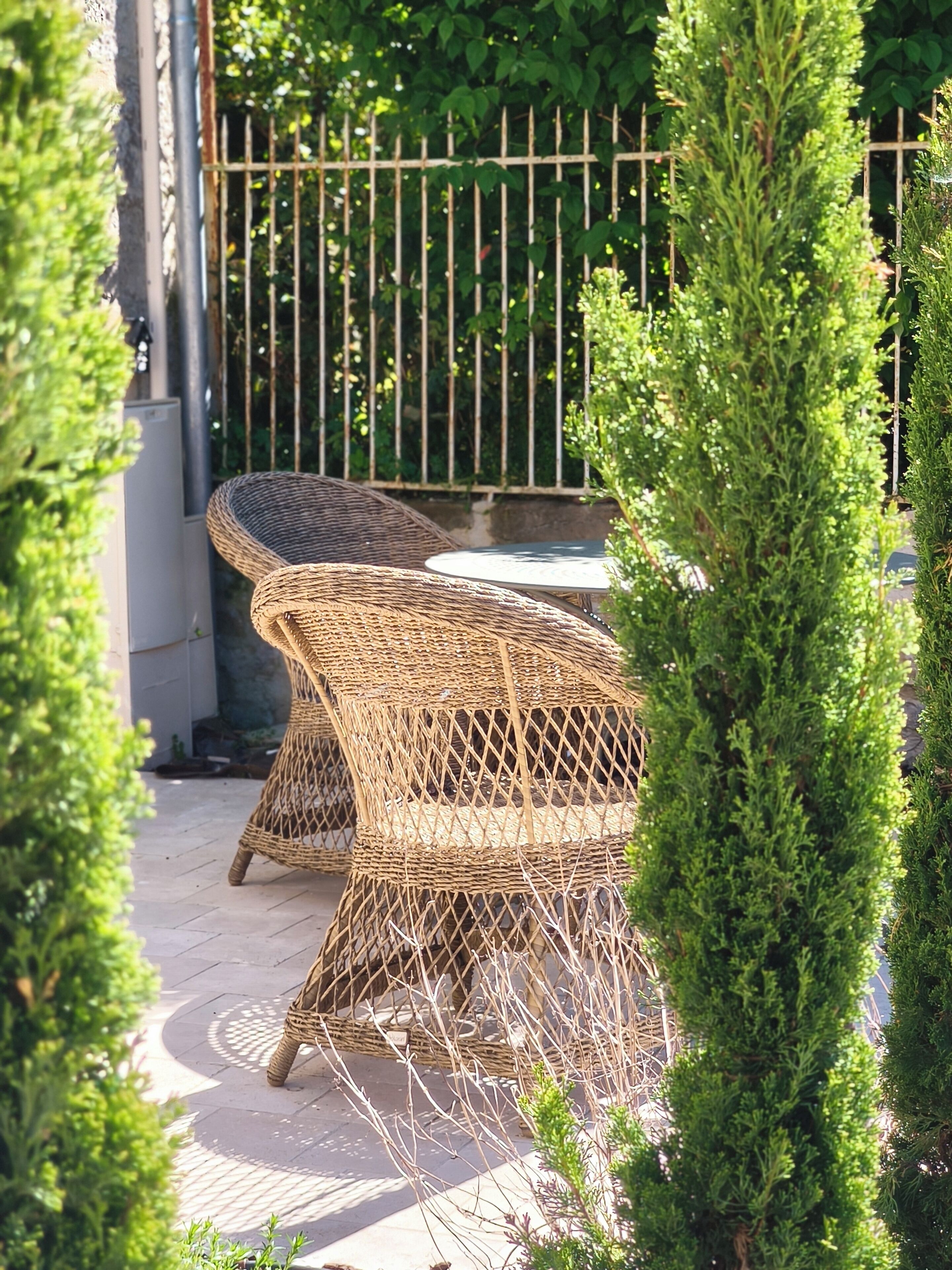 Mobilier d’extérieur en osier, une terrasse dallée et une clôture en métal.