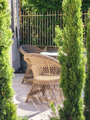 Wicker outdoor furniture, a paved patio, and a metal fence. - Hotel Maison Turenne (Martel)