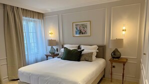 A well-appointed bedroom with a large bed, two bedside tables with lamps, a painting on the wall, and a window with curtains. - Hotel Maison Turenne (Martel)