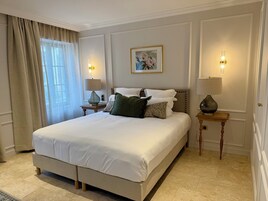 Un dormitorio elegante con una cama grande, dos mesitas de noche con lámparas, un cuadro en la pared y una ventana con cortinas.