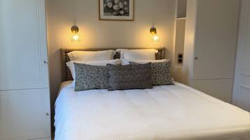 A neatly made bed with a headboard, two wall-mounted lamps, and a framed picture on the wall.