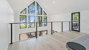Una habitación amplia con techo alto, ventanas grandes y un balcón con barandilla.