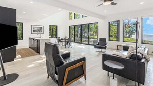 Amplia sala de estar con cocina, comedor y ventanas grandes que ofrecen vistas al exterior.