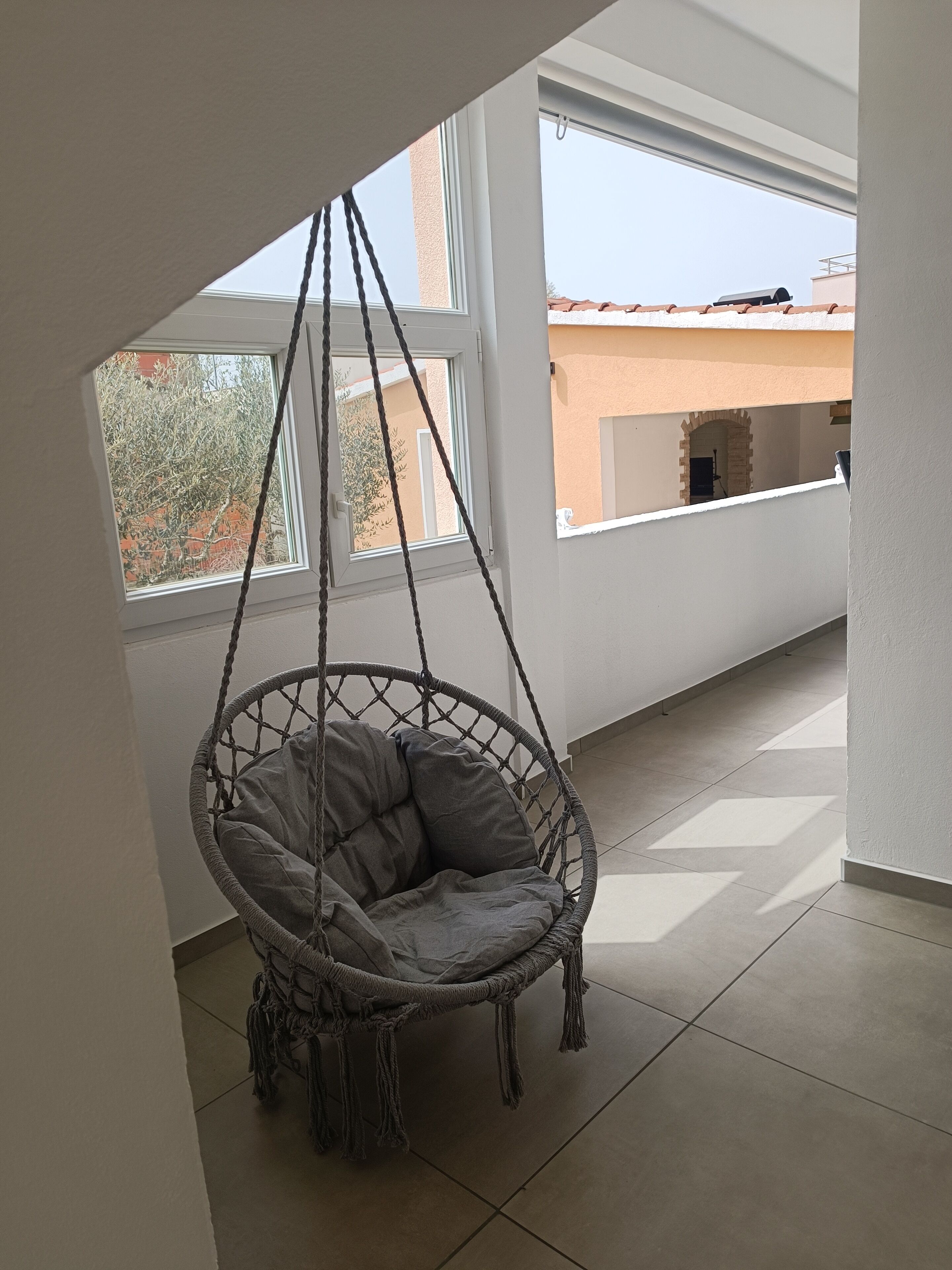 A room with a hanging chair, large windows, and a tiled floor.