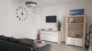 En moderne stue med en grå sofa, et rundt sofabord, en bogreol og et vægur.