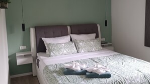 En pænt redt seng med mønstret sengetøj, et natbord med lampe, og en vægmonteret lampe.