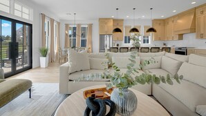 Een moderne keuken met houten kastjes, hangende lampen en een groot raam.