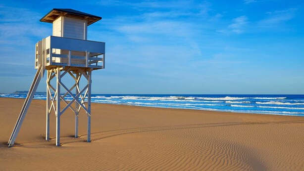 Ein Rettungsturm am sandigen Strand mit dem Meer im Hintergrund.