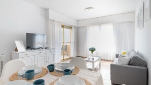 Ein modernes, gut beleuchtetes Wohnzimmer mit Essbereich, einer Couch und einem Fernseher auf einem Schrank.