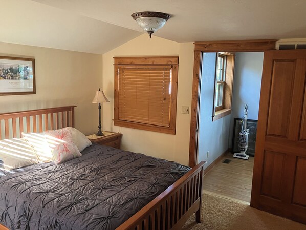 A bedroom with a bed, a nightstand, a lamp, a window with blinds, a ceiling light fixture, a mirror, and a door. - At The Bay. located on the beach. (Sturgeon Bay)