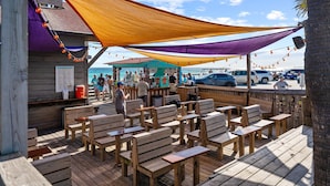 Eine Holzdielen-Terrasse mit Holzbänken und Tischen, ein Barbereich mit Theke und Blick auf den Ozean.