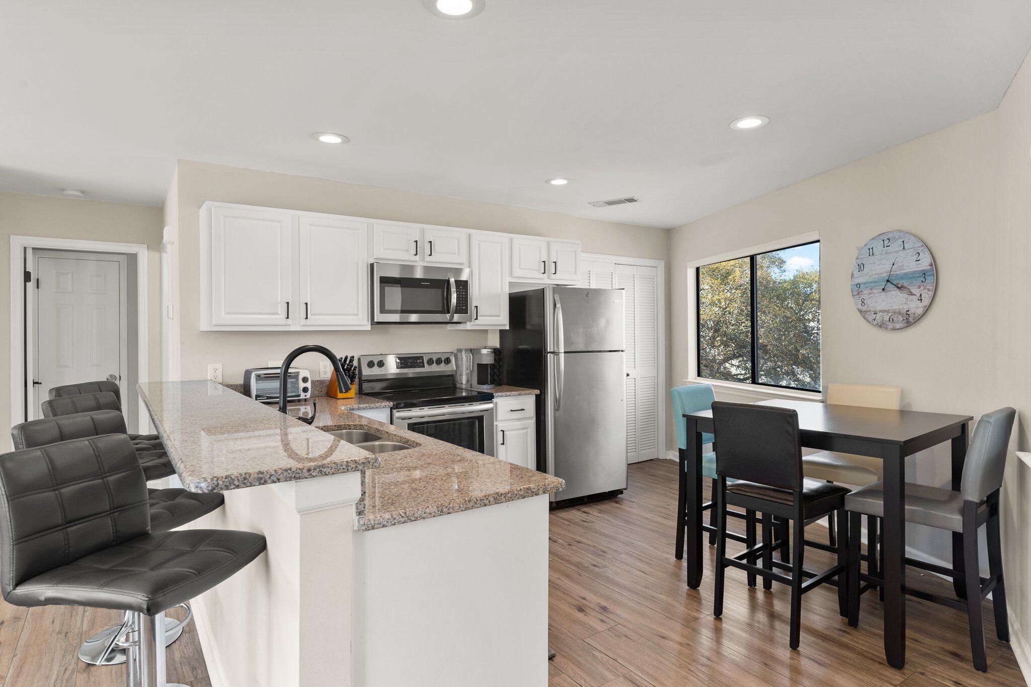A modern kitchen with white cabinets, stainless steel appliances, a granite countertop, and a dining area with a table and chairs.