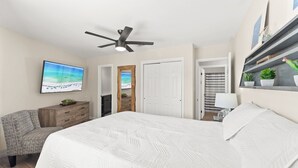 Ein Schlafzimmer mit einem großen Bett, einem Deckenventilator, einem Fernseher, einer Holzkabine und einer Tür zu einem weiteren Raum.