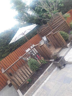 A patio area with a wooden fence, a white umbrella, and a planter with plants. - Carndonagh - 3-bedrooms - Sleeps 6/7 - Garden (Carndonagh)