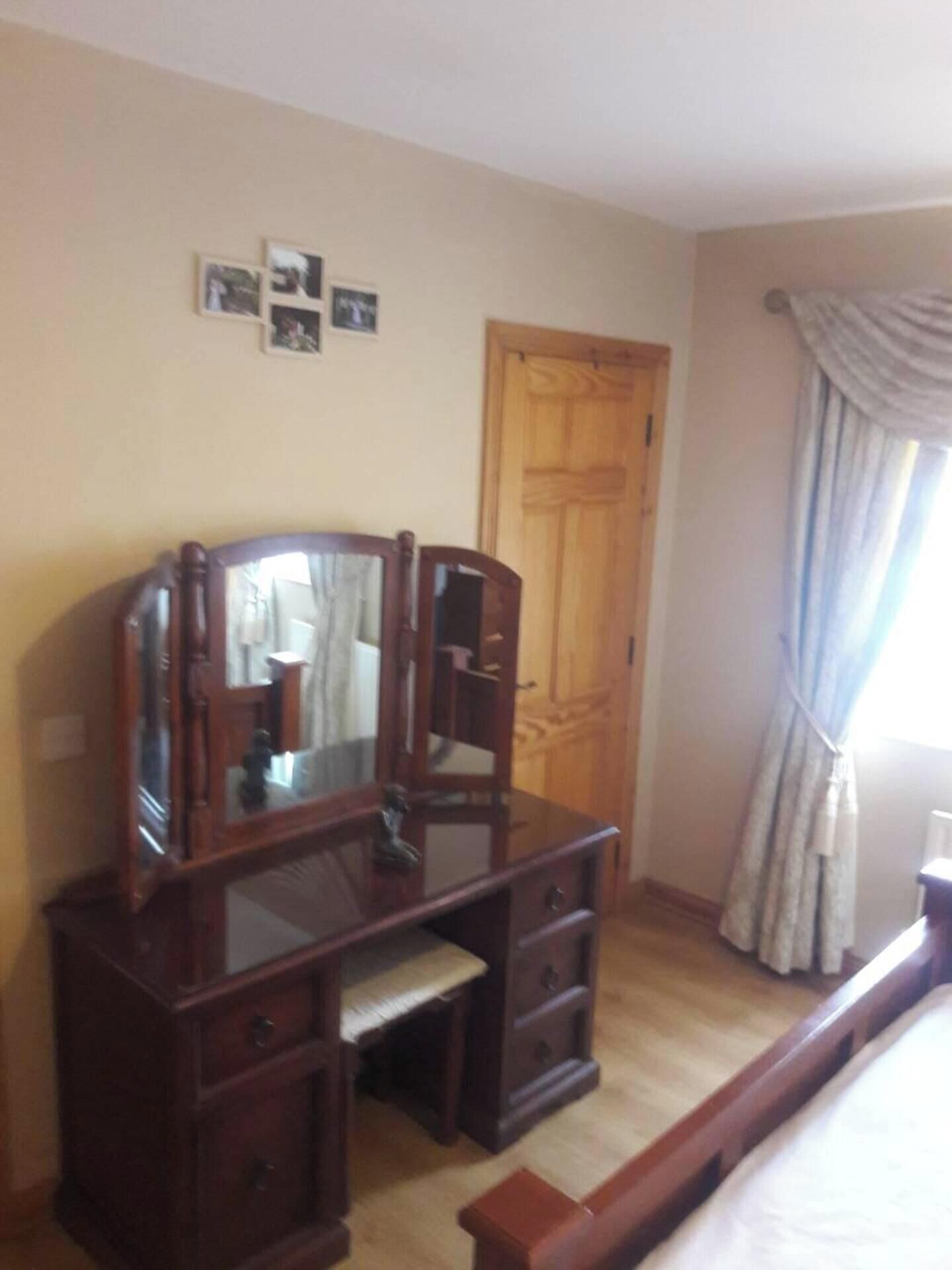 A bedroom with a wooden dresser, a mirror, a bed, a door, and a window with curtains.