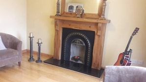 A living room with a fireplace, a sofa, a guitar, and two candle holders. - Carndonagh - 3-bedrooms - Sleeps 6/7 - Garden (Carndonagh)