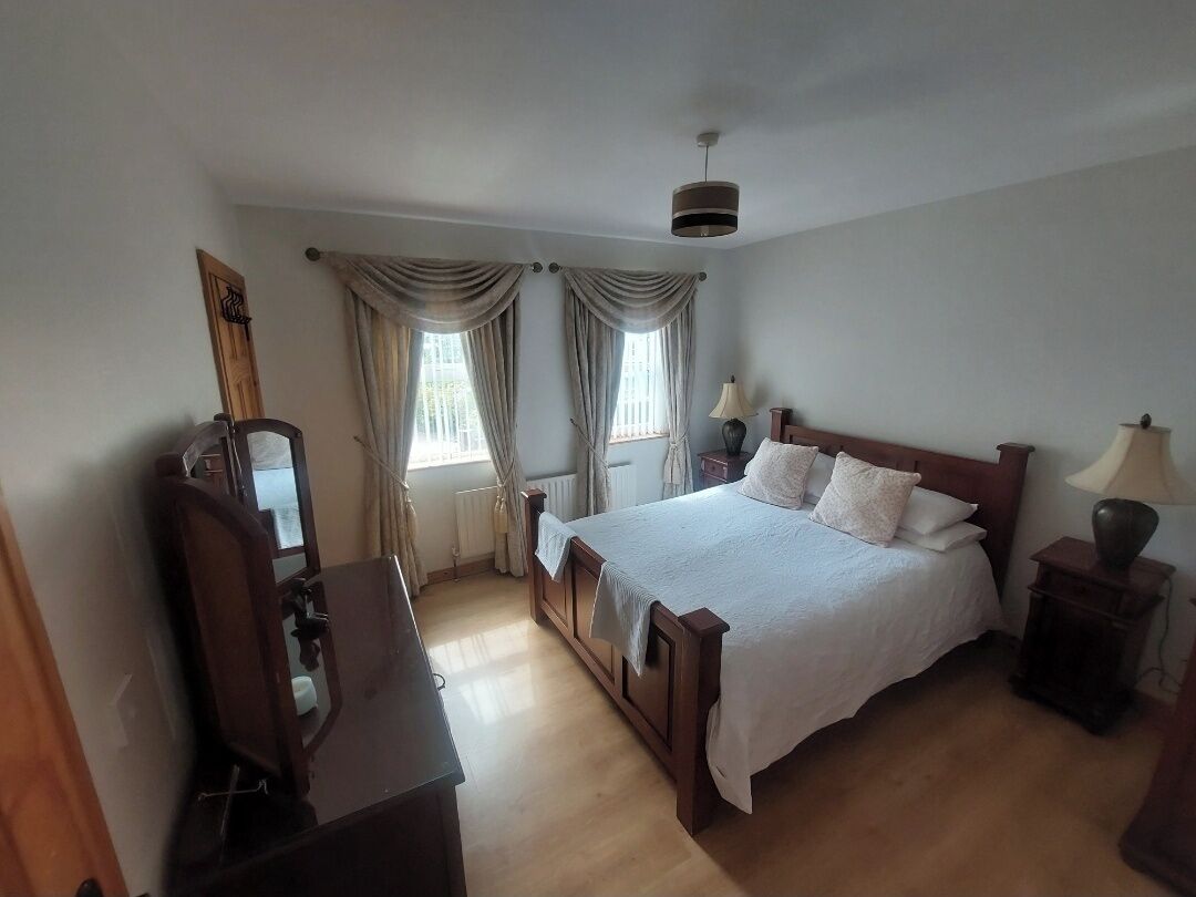 A bedroom with a wooden bed, two bedside tables, a nightstand, a desk, and a chair.