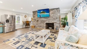 A modern living room with a stone fireplace, a flat-screen TV, a sofa, and a patterned rug. - Looking for a beach escape? Find out what Costal Corner has to offer your family (Oak Island)