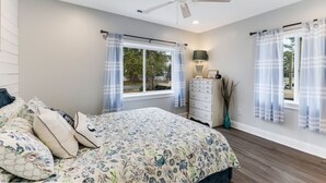 A bedroom with a bed, a dresser, a ceiling fan, and windows with curtains. - Looking for a beach escape? Find out what Costal Corner has to offer your family (Oak Island)