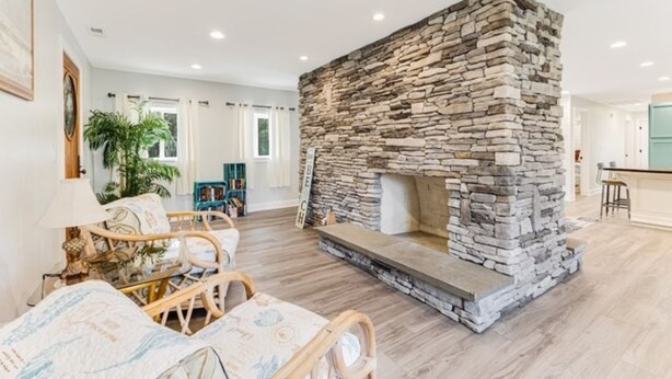 A living room with a stone fireplace, wicker furniture, and a large window. - Looking for a beach escape? Find out what Costal Corner has to offer your family (Oak Island)