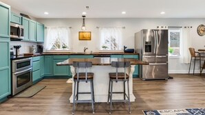 A modern kitchen with teal cabinets, stainless steel appliances, and a central island with bar stools. - Looking for a beach escape? Find out what Costal Corner has to offer your family (Oak Island)