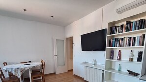 A room with a dining table, chairs, a bookshelf, a radiator, and a mounted TV.