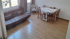 A room with a wooden floor, a sofa, a dining table with chairs, and a window with curtains.