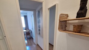 A hallway with wooden flooring, white walls, and a door leading to another room. There are woven baskets on a shelf and a small statue on the wall.