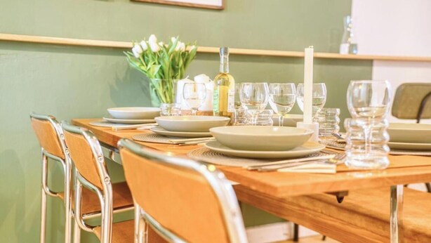 Una mesa de comedor dispuesta con platos, vasos y una vela, rodeada de sillas.