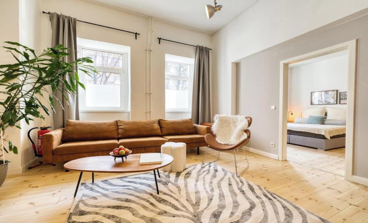 A spacious living room with a brown sofa, a round coffee table, a zebra-patterned rug, and a large potted plant.