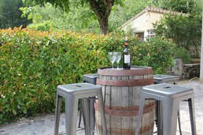 A rustic outdoor seating area with a wooden barrel centerpiece, two metal stools, and a bottle of wine. - Character house 10 minutes walk from the medieval village of Cajarc with swimming pool (Cajarc)