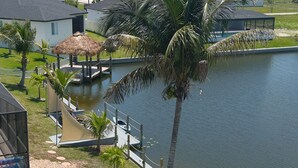 Een pand aan het water met een zwembad, palmbomen en een gazebo met rieten dak.