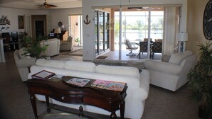 Een ruime woonkamer met een witte bank, een houten salontafel en een plafondventilator. Er is een glazen schuifdeur die leidt naar een balkon met buitenmeubilair.