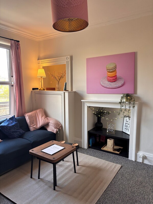 A cozy living room with a dark blue sofa, a small wooden table, and a pink-framed mirror.