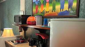 Una cocina equipada con microondas, tostadora, cafetera y refrigerador. Hay un cuadro sobre el fregadero y una lámpara en la encimera.