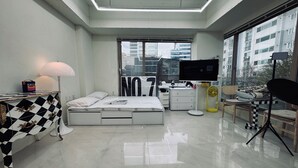 Un dormitorio moderno con cama, mesita de noche, lámpara, cómoda, televisor y ventanas amplias.