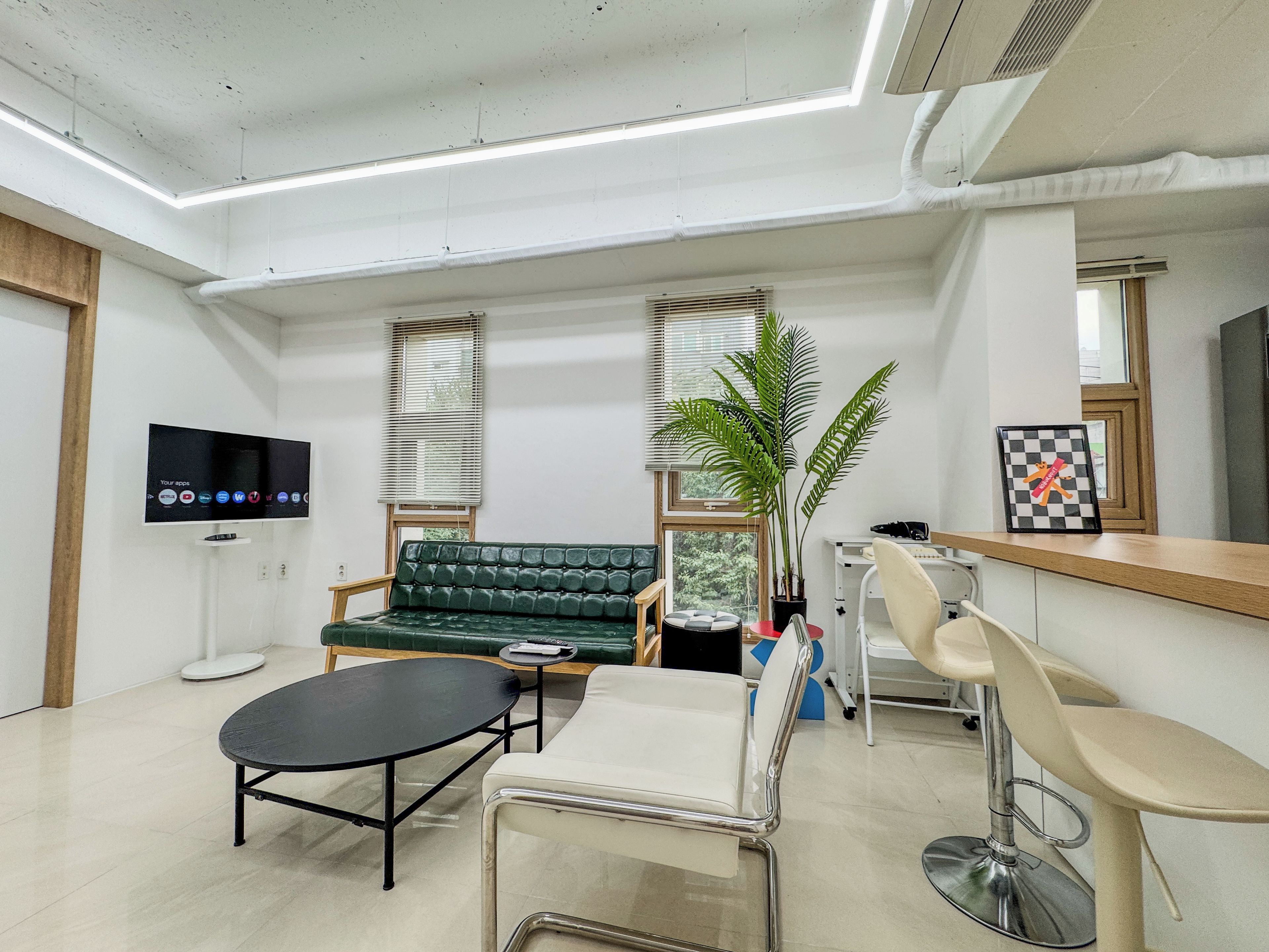 A modern waiting area with a sofa, a round table, a bar area, and a television mounted on the wall.